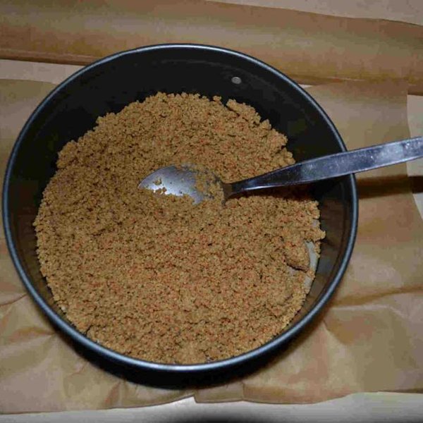 Druk met een lepel het muesli-botermengsel stevig plat in de springvorm. Dit wordt de bodem van de taart